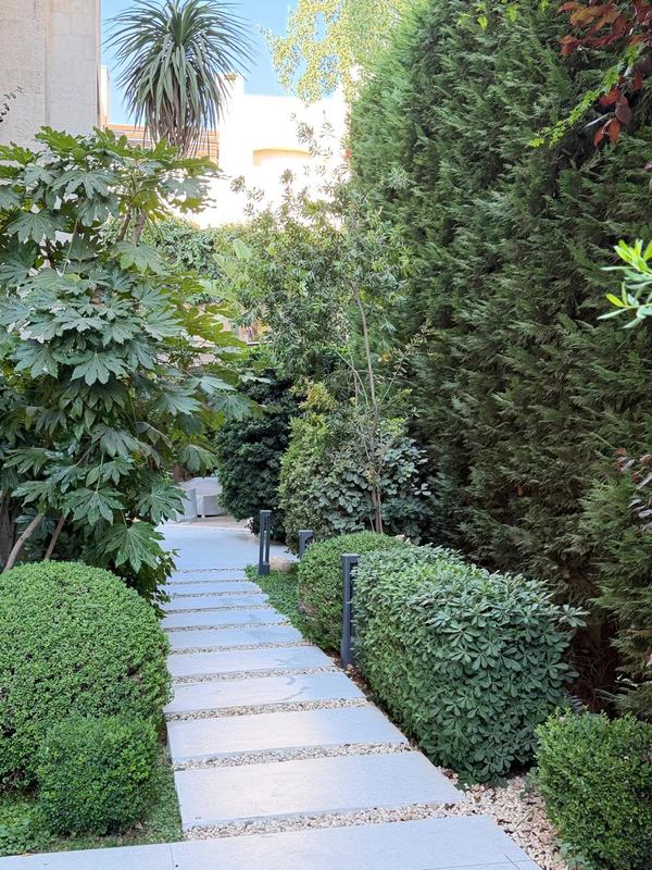 A path of pale stone slabs with gravel joints, lined with clipped shrubs and low bollard lights.