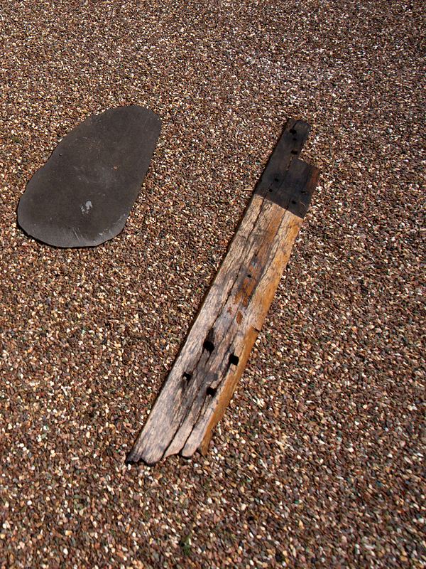 A dark basalt stepping stone beside a weathered timber plank, set in mixed gravel.